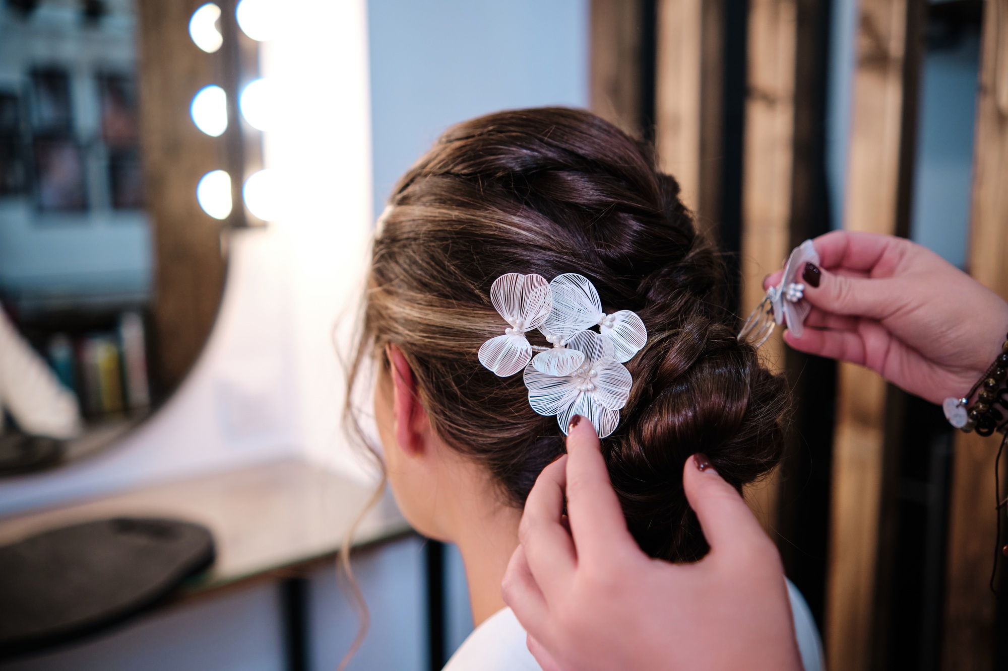Stylist attachs hair accessories on her client while doing her wedding hairstyle at the hair salon.