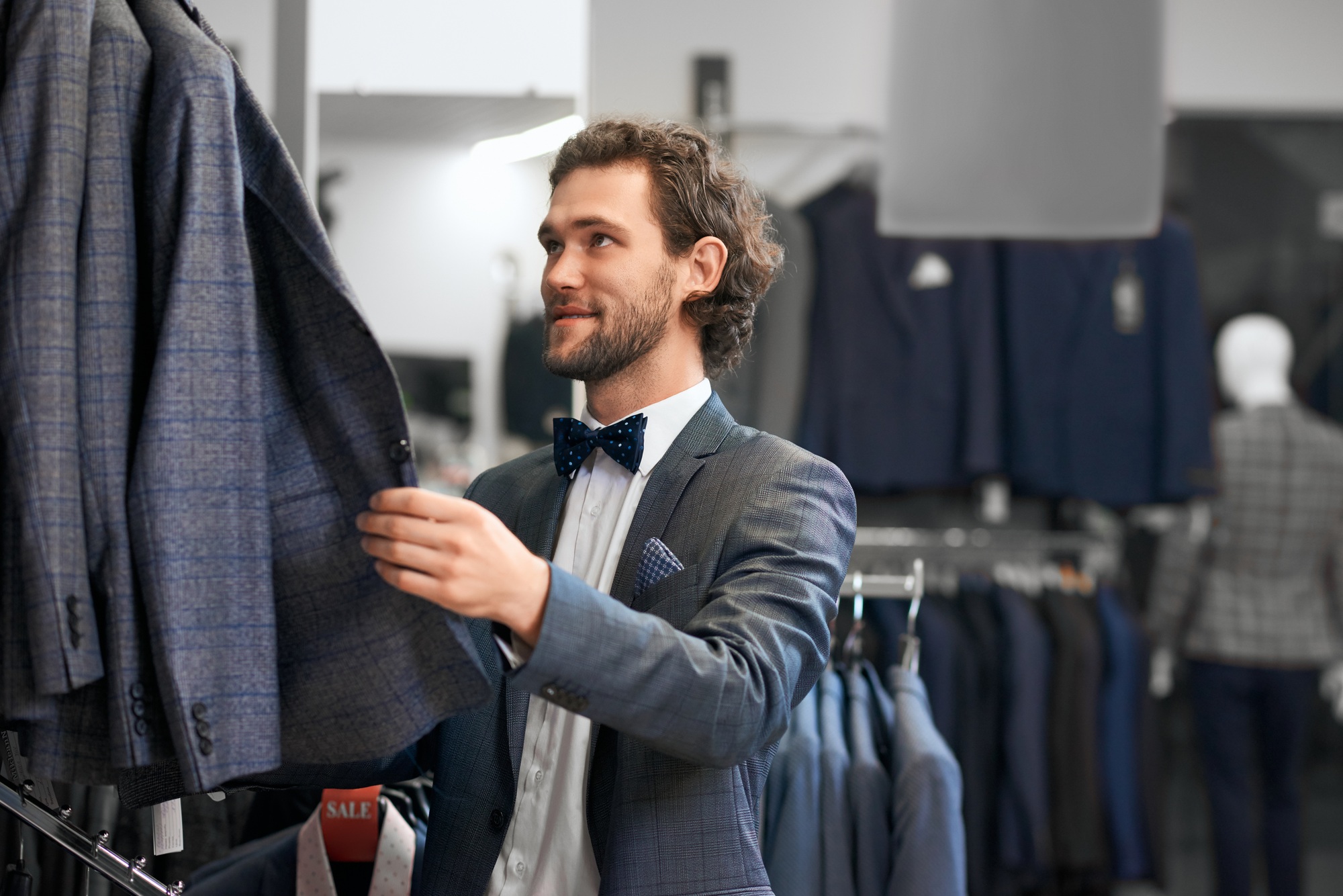 Young man choosing suits in boutique