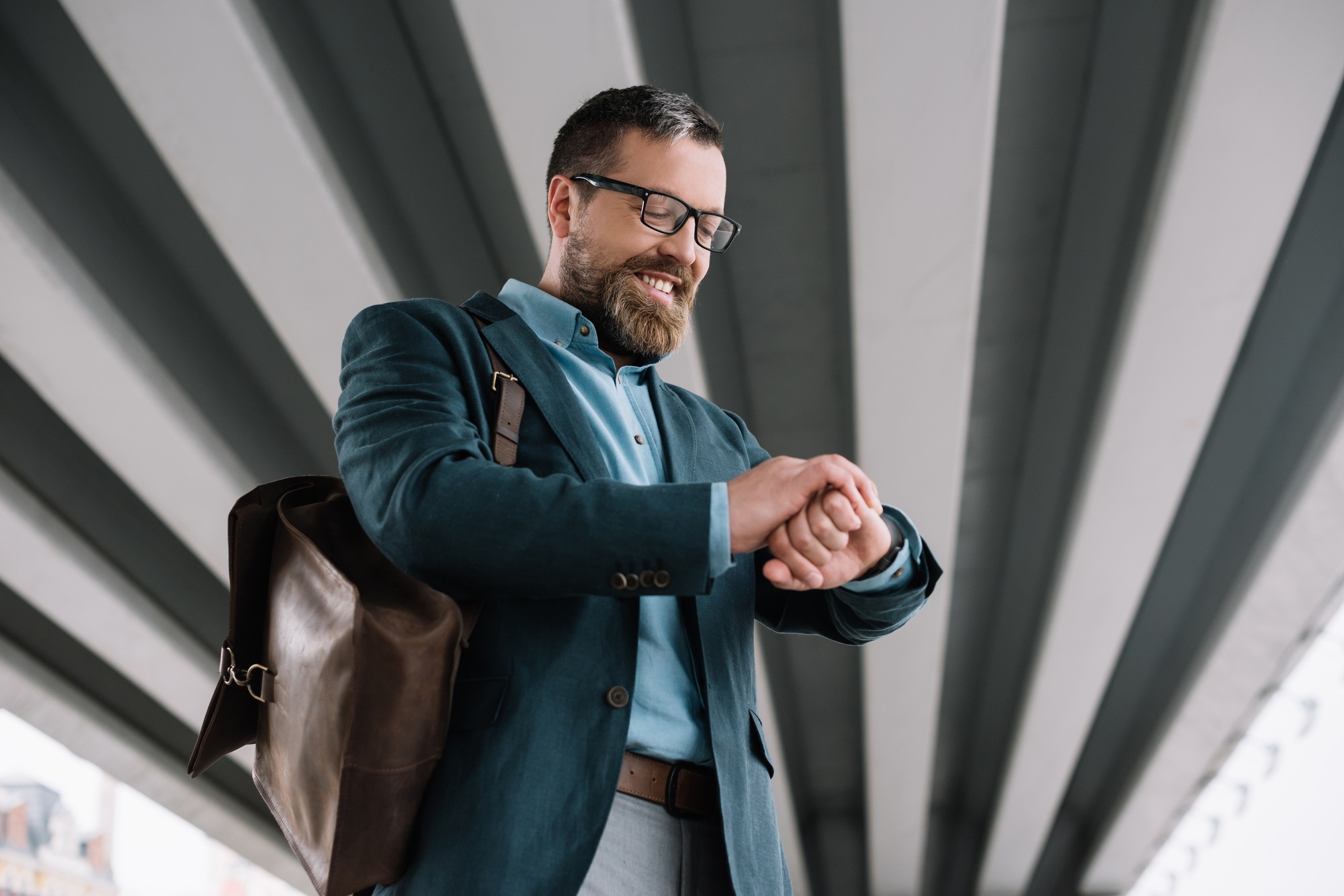 bottom view of beard stylish businessman with leather bag looking at wristwatch