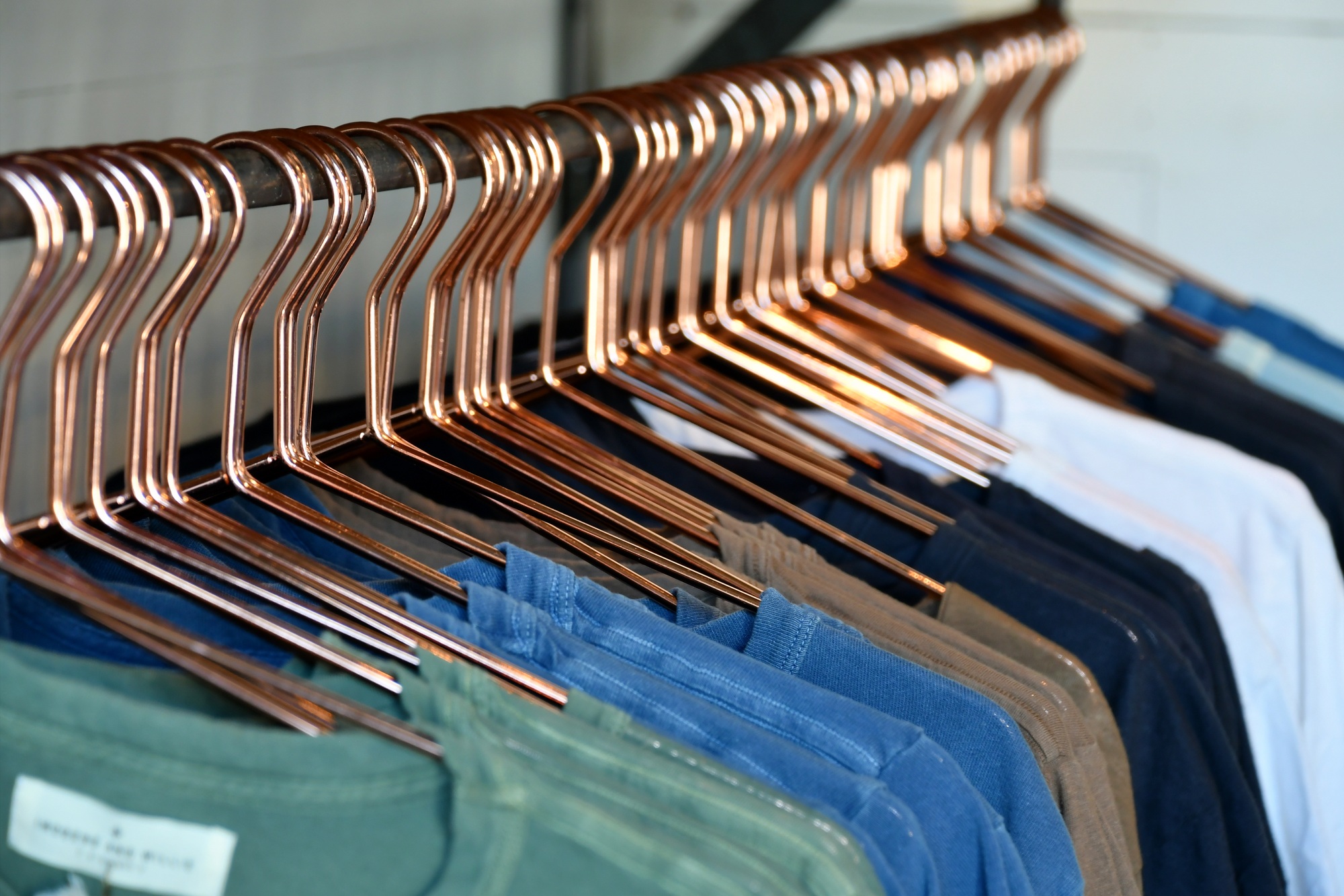 Colorful array of t-shirts on brass hangers in clothing store for purchase by shoppers shop buy sell